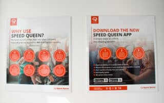 Two posters on a wall promoting the new Speed Queen app with the message "Download the new Speed Queen app.