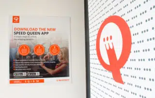 A wall poster displaying the message: "Download the new Speed Queen app" in bold, eye-catching typography
